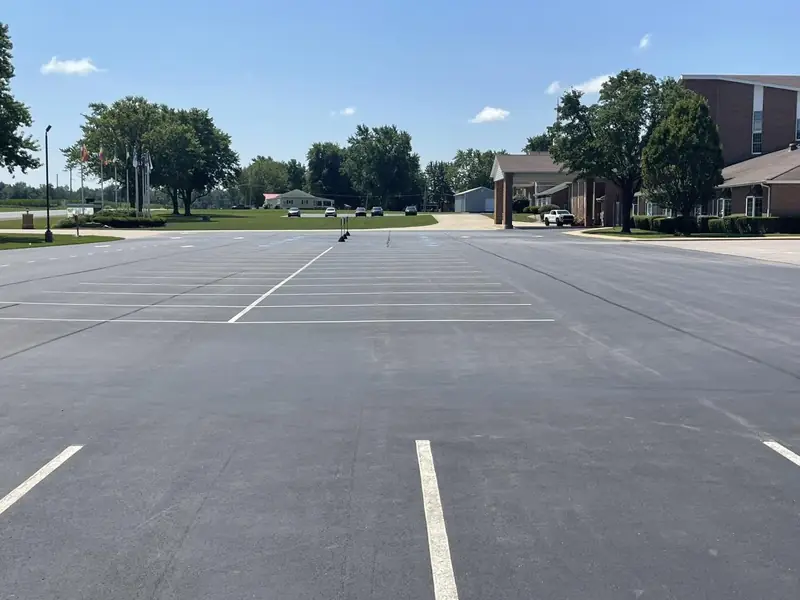 Wide parking lot with new white stall lines beside brick campus buildings