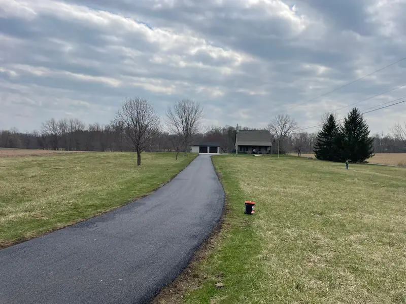 Long new asphalt driveway running across a field to a farmhouse