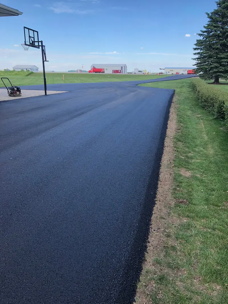 Finished asphalt driveway with clean edges running past a basketball hoop toward the road