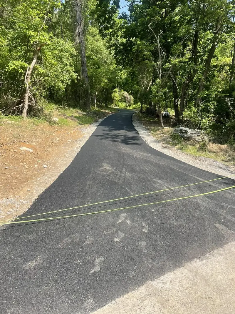 Fresh asphalt climbing a wooded hillside, string lines still set along the edge
