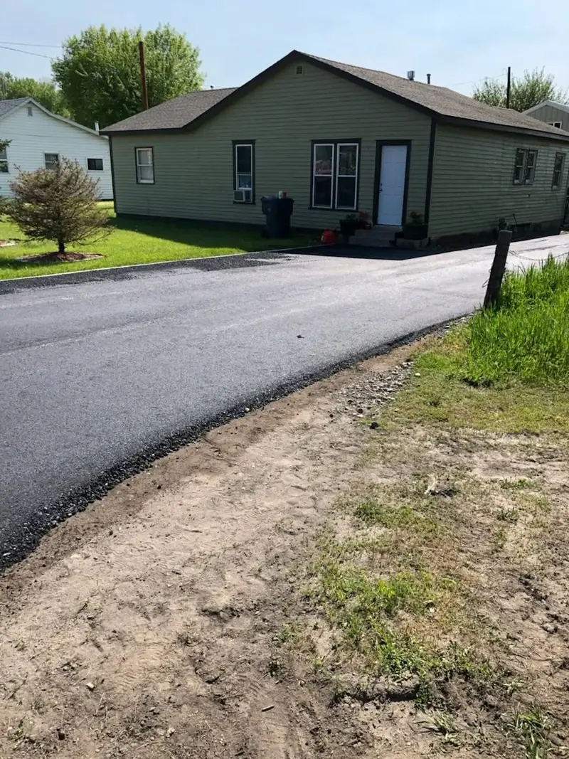 New asphalt drive and parking apron in front of a green-sided house