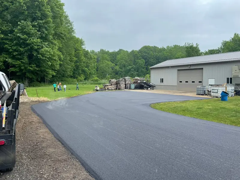 Fresh asphalt drive and turnaround curving up to a large pole barn