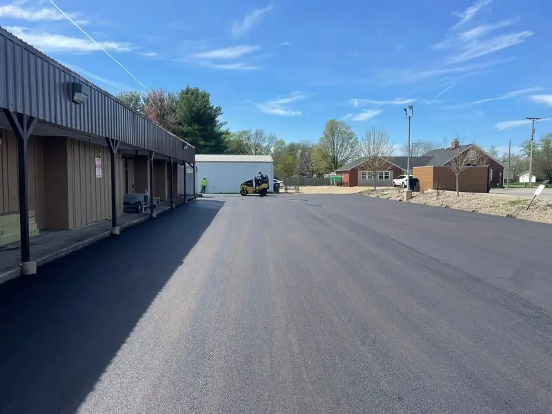 Long new asphalt drive along a row of storage units, with the roller finishing at the far end