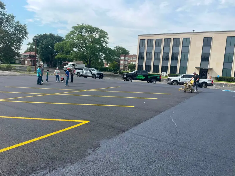 Crew painting new yellow stall lines on an office parking lot with a walk-behind striper
